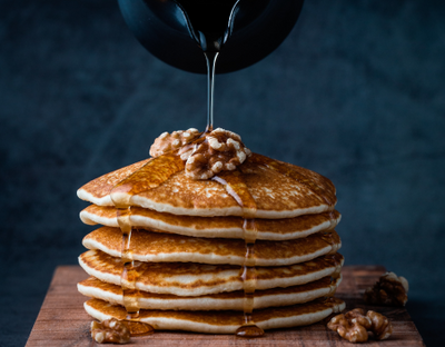 Stack of pancakes with walnuts on top and maple syrup poured over